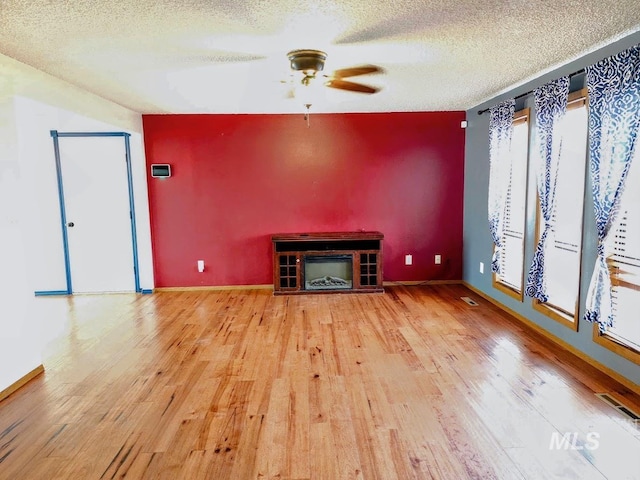 unfurnished living room featuring ceiling fan, wood-type flooring, and a textured ceiling