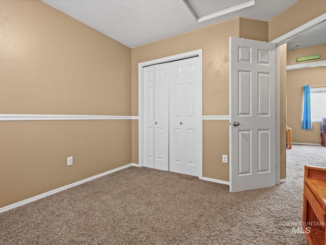 unfurnished bedroom featuring baseboards, attic access, carpet floors, and a closet