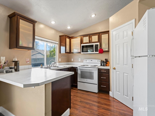 kitchen with a sink, light countertops, dark wood finished floors, white appliances, and a peninsula
