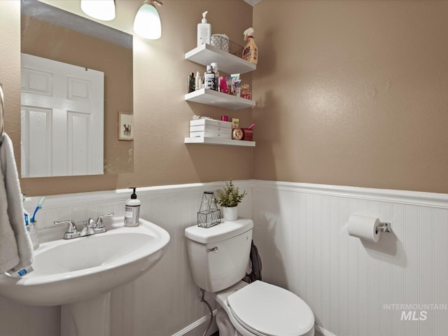 bathroom with wainscoting, toilet, and a sink