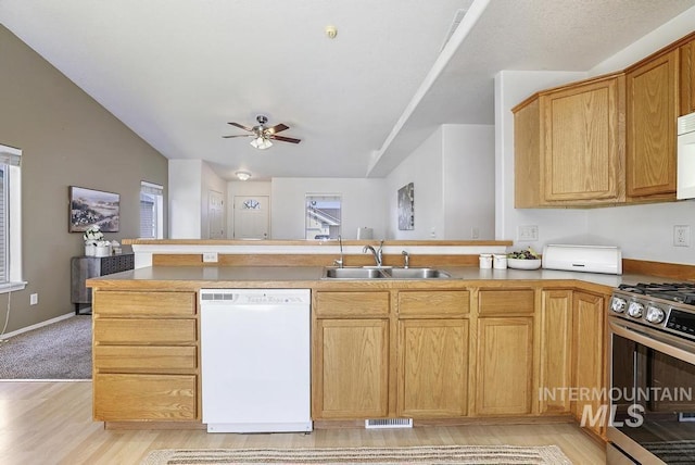 kitchen with visible vents, a sink, white appliances, a peninsula, and light wood-style flooring