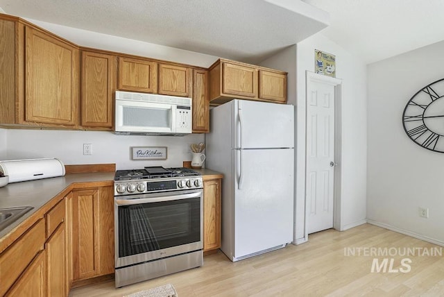kitchen featuring dark countertops, brown cabinets, white appliances, light wood-type flooring, and lofted ceiling