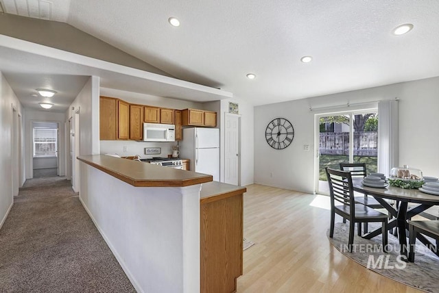 kitchen featuring brown cabinets, lofted ceiling, white appliances, baseboards, and a peninsula
