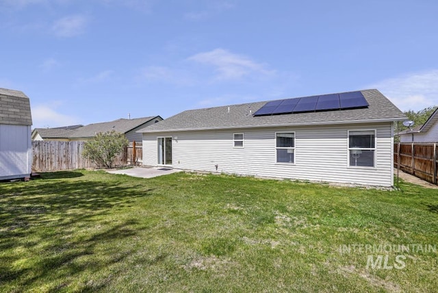 back of property featuring roof mounted solar panels, a fenced backyard, roof with shingles, and a yard