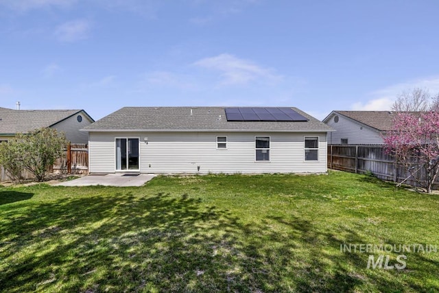 back of house with roof mounted solar panels, a patio area, a fenced backyard, and a lawn