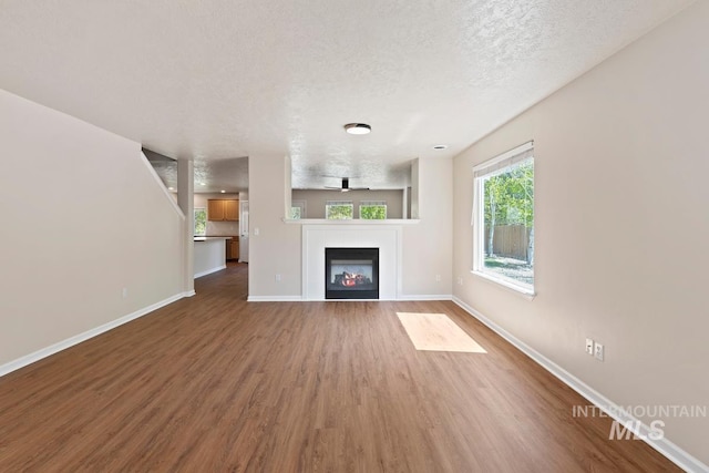 7362 S Shadowmoss Ave, Boise, ID 83709 - unfurnished living room with a textured ceiling, wood finished floors, baseboards, and a glass covered fireplace