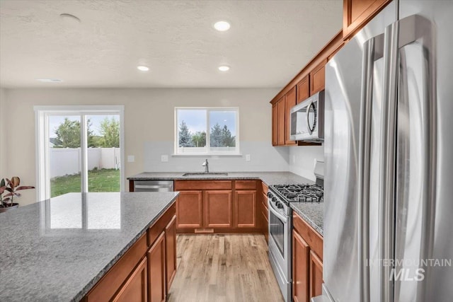 kitchen with stainless steel appliances, a sink, brown cabinets, light stone countertops, and recessed lighting