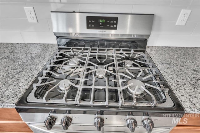 kitchen view of stainless steel gas range oven, decorative backsplash, and stone countertops