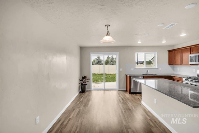 kitchen featuring a sink, appliances with stainless steel finishes, wood finished floors, baseboards, and brown cabinetry