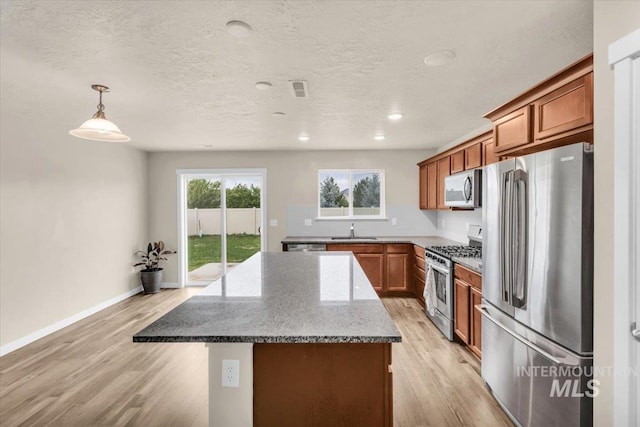 kitchen with stainless steel appliances, a kitchen island, brown cabinetry, light wood finished floors, and a textured ceiling