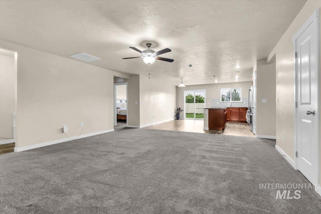 unfurnished living room with carpet, ceiling fan, baseboards, and a textured ceiling