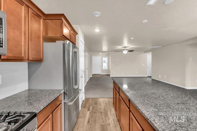 kitchen featuring brown cabinets, ceiling fan, stone counters, tasteful backsplash, and open floor plan