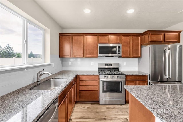 kitchen featuring appliances with stainless steel finishes, a sink, light stone countertops, brown cabinets, and recessed lighting