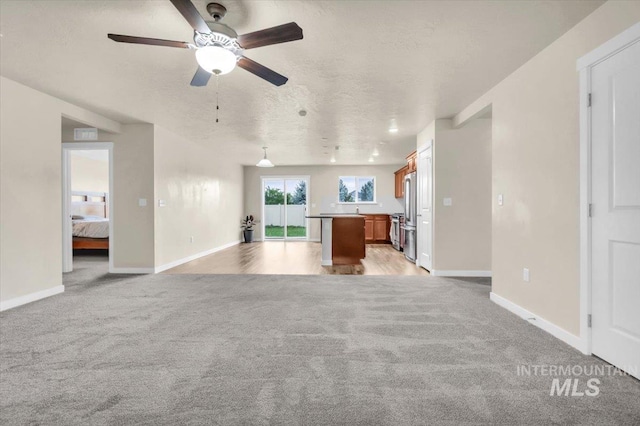 unfurnished living room with light carpet, ceiling fan, baseboards, and a textured ceiling