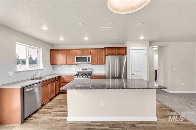 kitchen featuring appliances with stainless steel finishes, a sink, a kitchen island, brown cabinetry, and recessed lighting
