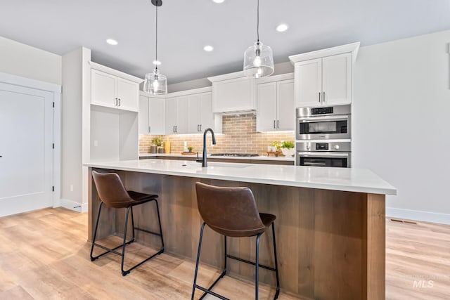 1501 E Andes Dr, Kuna, ID 83634 - kitchen featuring stainless steel double oven, white cabinets, decorative backsplash, light wood finished floors, and cooktop