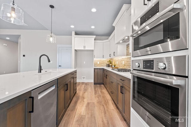 1501 E Andes Dr, Kuna, ID 83634 - kitchen with stainless steel appliances, light wood-style flooring, white cabinets, decorative backsplash, and decorative light fixtures