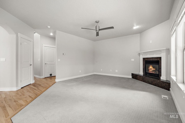 living room featuring a high end fireplace, visible vents, ceiling fan, baseboards, and a textured ceiling