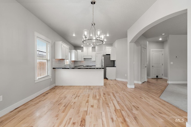 kitchen featuring dark countertops, backsplash, open floor plan, freestanding refrigerator, and arched walkways