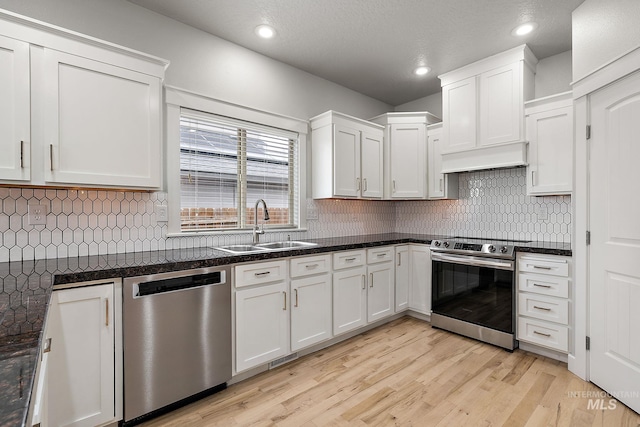 kitchen with a sink, stainless steel appliances, white cabinets, light wood-type flooring, and backsplash