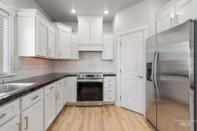 kitchen featuring light wood finished floors, backsplash, appliances with stainless steel finishes, white cabinets, and a sink