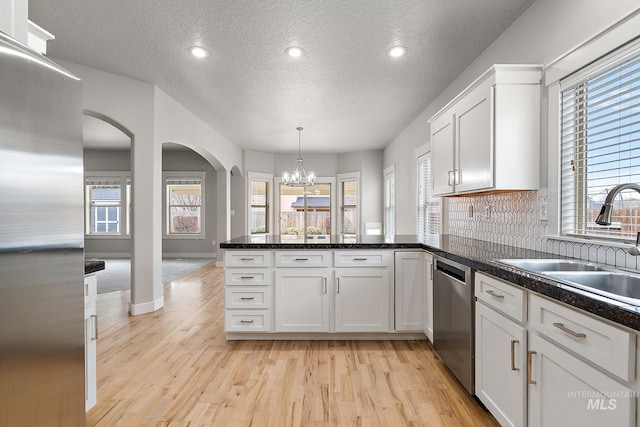 kitchen featuring light wood finished floors, a peninsula, white cabinets, stainless steel appliances, and a sink