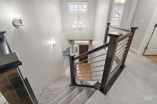 stairway featuring plenty of natural light, a towering ceiling, an inviting chandelier, and carpet floors