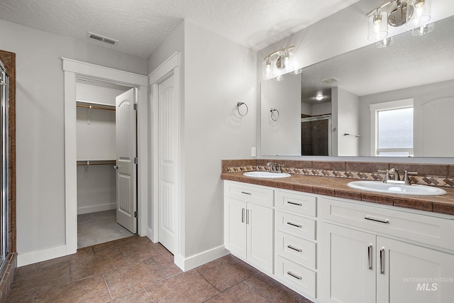 bathroom with a sink, visible vents, a stall shower, and double vanity