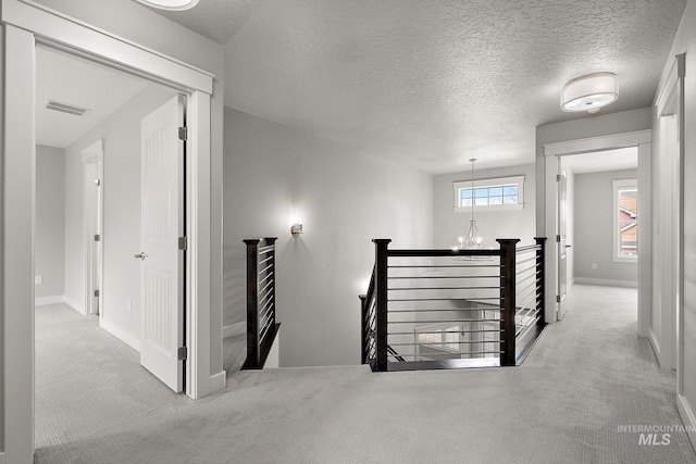 hall featuring visible vents, an upstairs landing, a textured ceiling, an inviting chandelier, and carpet flooring