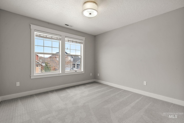 carpeted spare room featuring visible vents, baseboards, and a textured ceiling