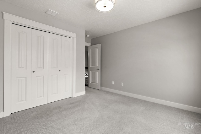 unfurnished bedroom featuring visible vents, baseboards, a closet, a textured ceiling, and light carpet