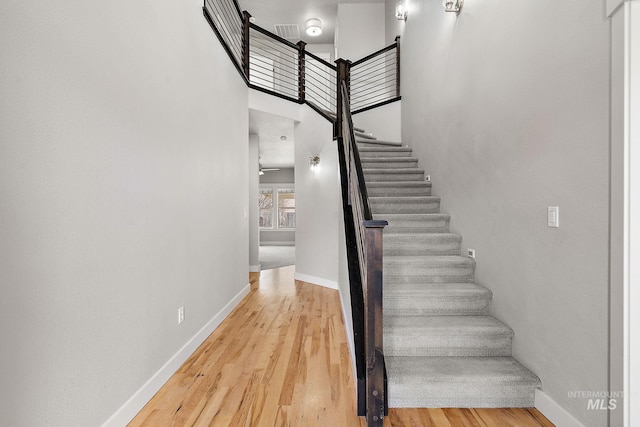 stairway with a towering ceiling, visible vents, baseboards, and wood finished floors