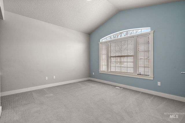 spare room with visible vents, a textured ceiling, carpet floors, baseboards, and vaulted ceiling