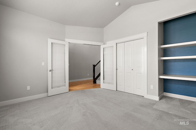 unfurnished bedroom with baseboards, lofted ceiling, carpet flooring, french doors, and a closet