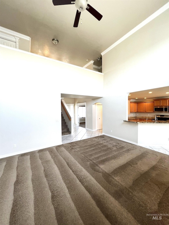 unfurnished living room with a high ceiling, ceiling fan, and light colored carpet