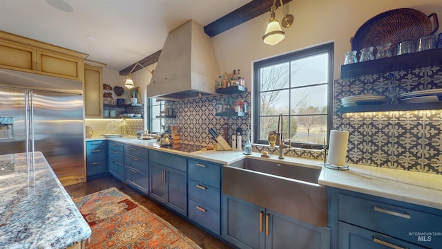 kitchen featuring custom range hood, built in refrigerator, blue cabinets, and open shelves