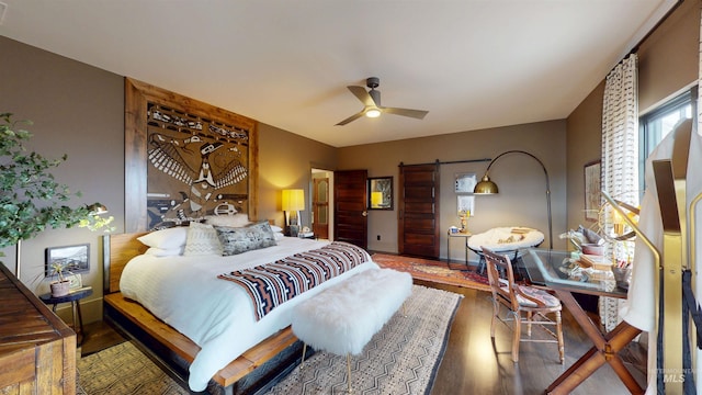 bedroom with a barn door, wood finished floors, and a ceiling fan
