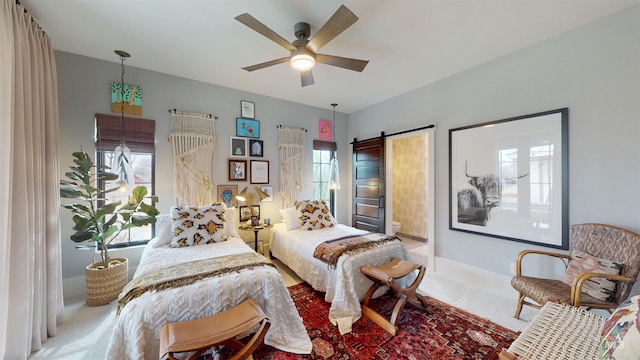 carpeted bedroom with baseboards, a barn door, ensuite bathroom, and a ceiling fan