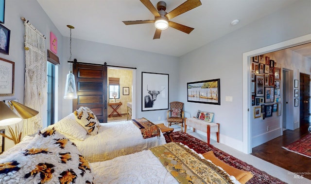 bedroom with baseboards, a barn door, ceiling fan, and ensuite bath