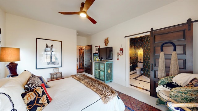 carpeted bedroom with a barn door, connected bathroom, and a ceiling fan