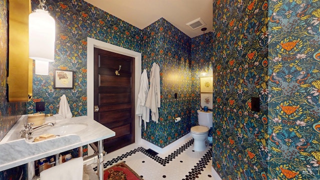 bathroom featuring visible vents, wallpapered walls, toilet, a sink, and tile patterned flooring