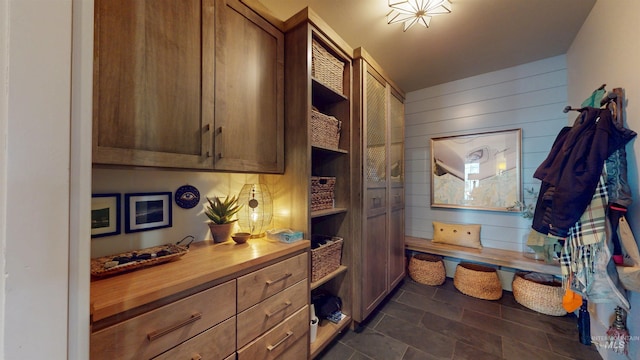 kitchen with brown cabinetry, wood counters, wooden walls, and open shelves