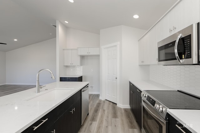 kitchen featuring light wood-style flooring, dark cabinetry, a sink, white cabinetry, and appliances with stainless steel finishes