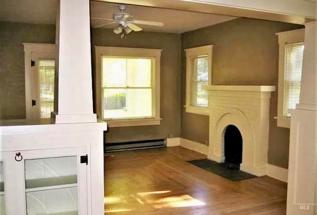 unfurnished living room with ceiling fan, a baseboard heating unit, a wealth of natural light, and dark hardwood / wood-style flooring