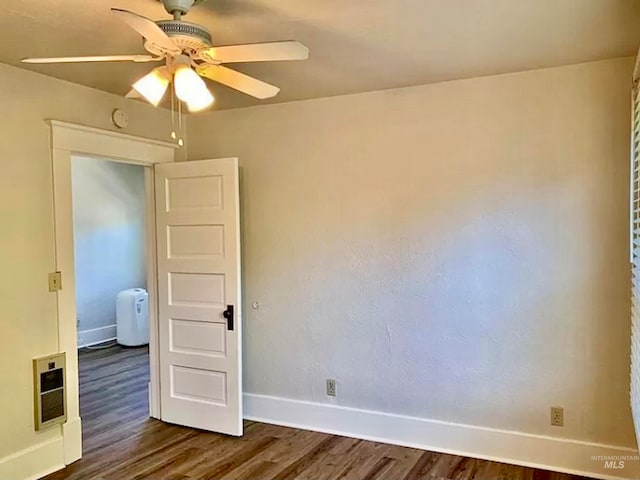 spare room with ceiling fan, heating unit, and dark hardwood / wood-style flooring