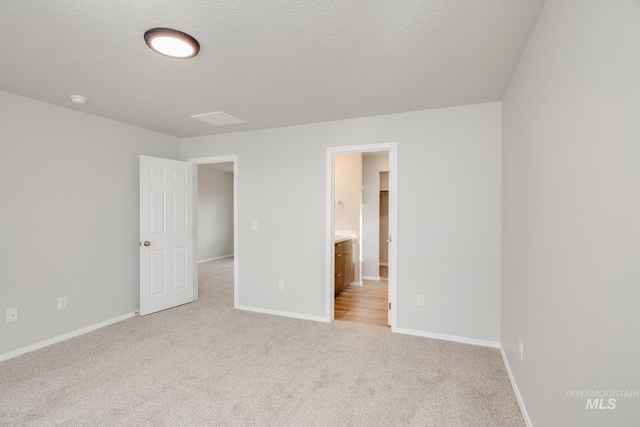 unfurnished bedroom with a textured ceiling, connected bathroom, and light colored carpet