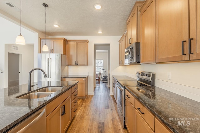 kitchen featuring pendant lighting, sink, light hardwood / wood-style flooring, appliances with stainless steel finishes, and dark stone counters