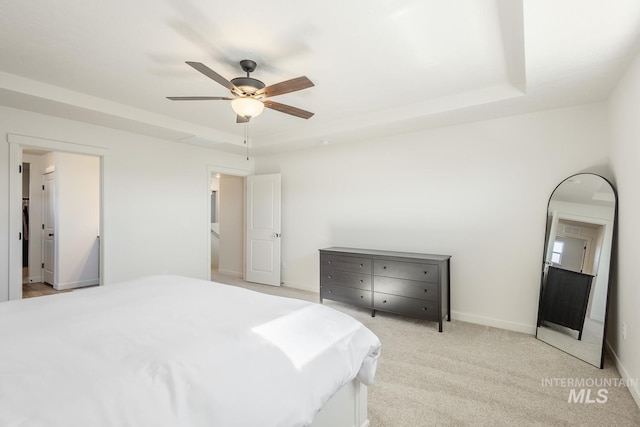 bedroom with light carpet, a tray ceiling, and ceiling fan