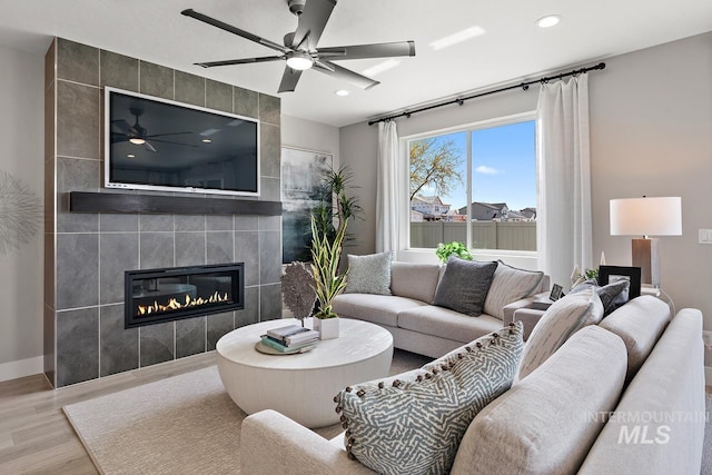 living room featuring ceiling fan, light hardwood / wood-style flooring, tile walls, and a tiled fireplace