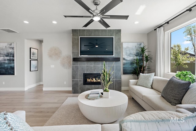 living room featuring ceiling fan, light hardwood / wood-style flooring, tile walls, and a fireplace